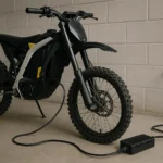 electric dirt bike charging tips showing a realistic off-road bike plugged into a wall outlet in a garage environment